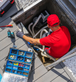 A man in red shirt holding tools near an open hatch.